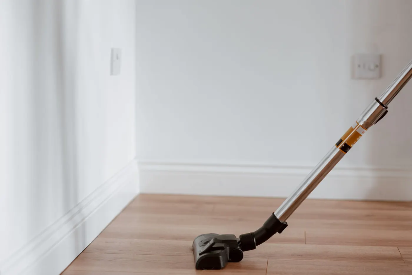 Brosse d'aspirateur passée le long d'une plinthe blanche, sur un sol en bois clair