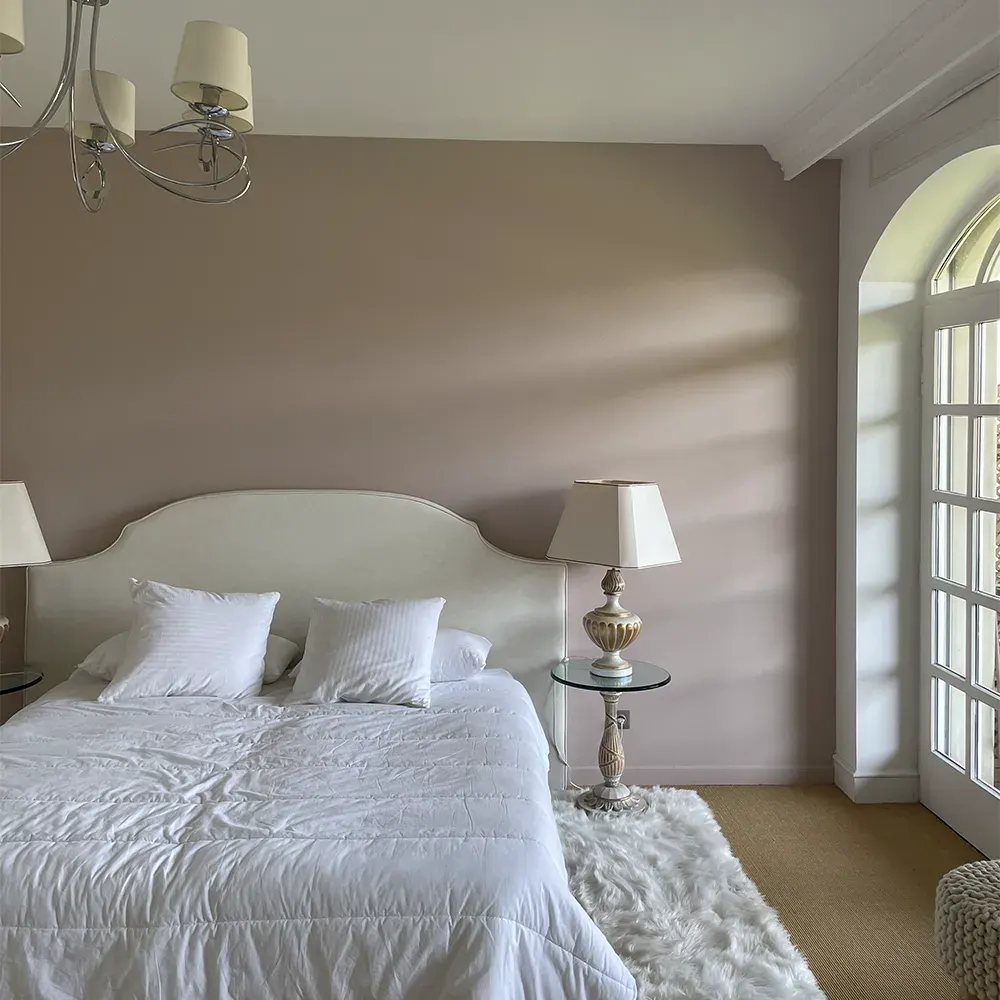 Chambre claire au soleil, tête de lit capitonnée, linge blanc et porte-fenêtre en arc
