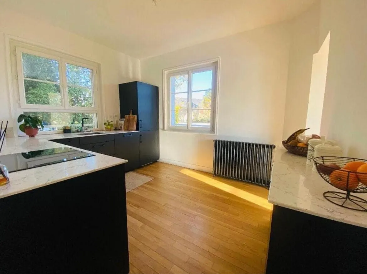 Cuisine au soleil, façades noires, plans de travail effet marbre et parquet de chêne