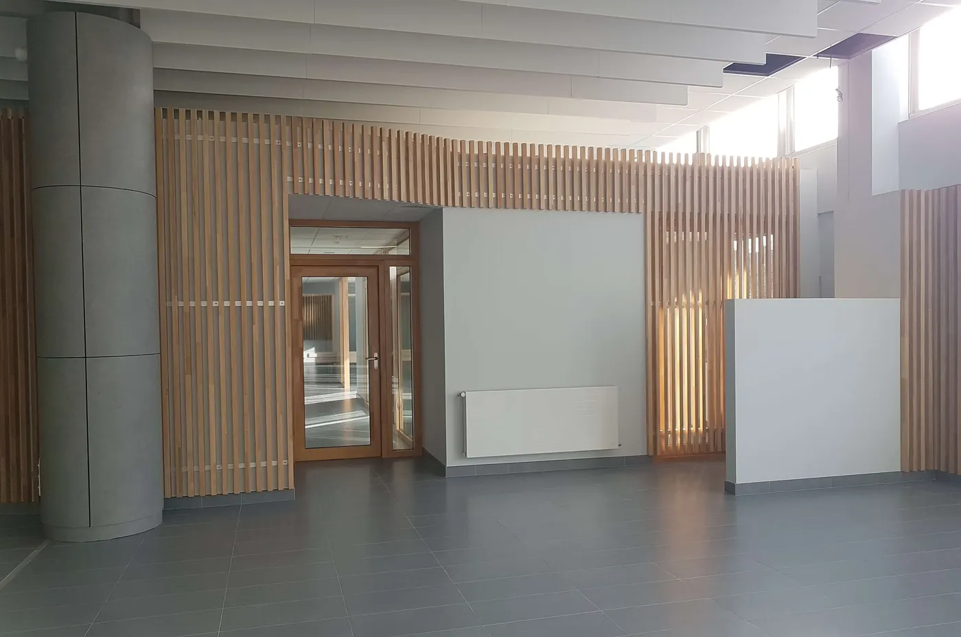 Hall de bureaux vide, claustra en lattes de bois et carrelage gris net