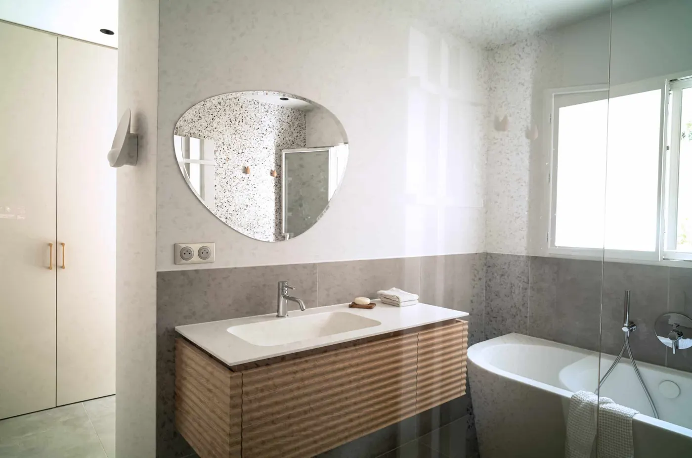 Salle de bain claire en terrazzo, miroir rond, meuble cannelé en chêne et baignoire